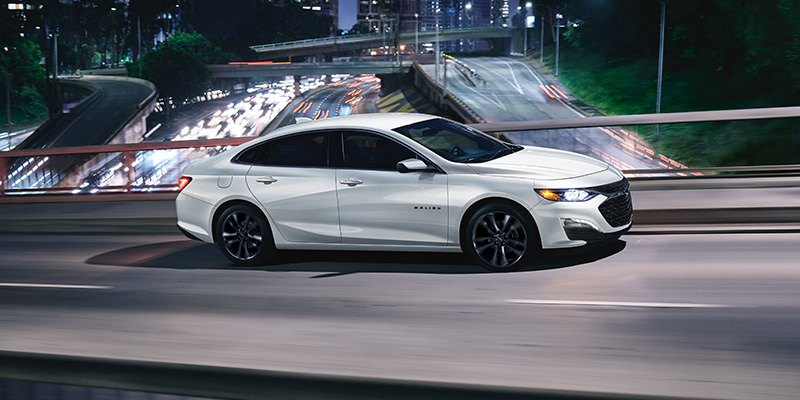 a white 2025 Chevrolet Malibu driving across a city bridge