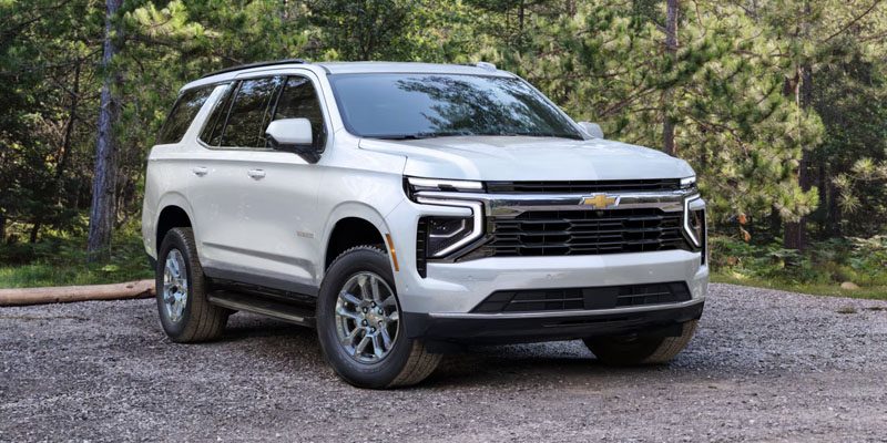 a white 2025 Chevrolet Tahoe parked on a gravel patch in a wooded area